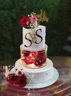 a three tiered wedding cake with red roses on the bottom and gold lettering that says s & s