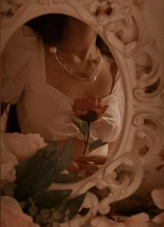 a woman is holding a rose in front of a mirror with flowers around her neck