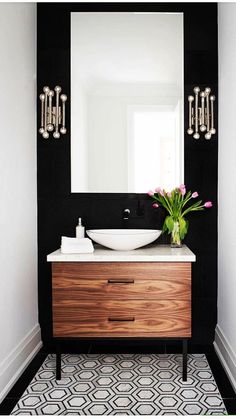 a bathroom with black and white tile, wooden cabinet, sink and mirror on the wall