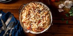 a dish of pasta with cheese and tomatoes on a wooden table next to silverware