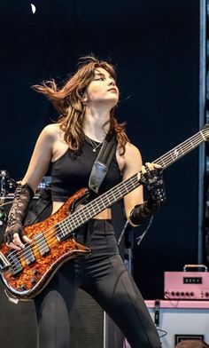 a woman with long hair playing a bass guitar on stage at a music festival or concert