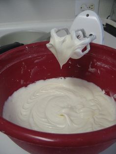 a red bowl filled with whipped cream on top of a stove