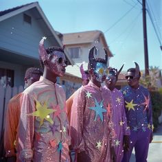 men in pink and purple costumes with stars painted on their faces are standing outside the house