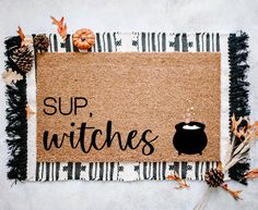 a door mat with the words sup witches on it next to pumpkins and pine cones