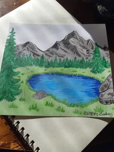 a drawing of a lake surrounded by mountains and pine trees on a paper with colored pencils