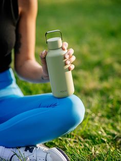 a woman sitting on the grass holding a water bottle in one hand and wearing blue leggings