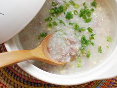 a white bowl filled with meat and rice next to a wooden spoon on top of a table