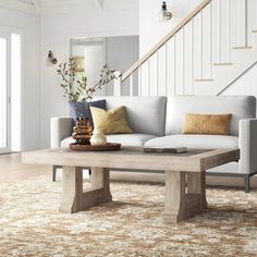 a living room with a couch, coffee table and stair case in the background on an area rug