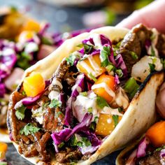 two tacos filled with meat and veggies being held by someone's hand