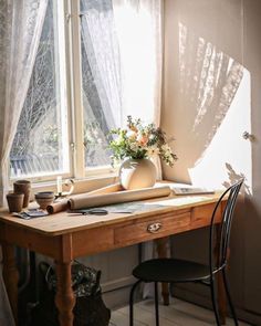 a wooden desk sitting in front of a window next to a vase filled with flowers