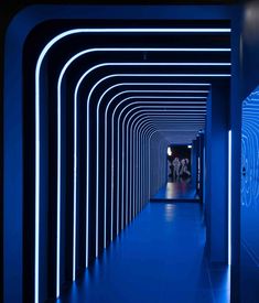 an empty hallway with blue lighting and people walking down the corridor between it to another room