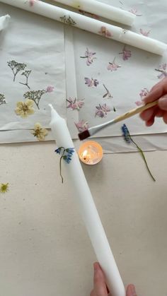 someone is painting flowers on the wall with white paint and a candle in front of them