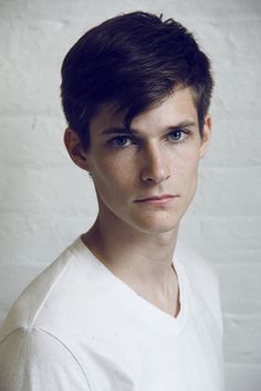 a young man with short hair wearing a white t - shirt and looking at the camera