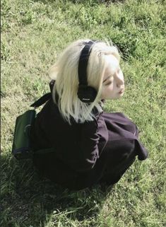 a blonde doll with headphones sitting in the grass