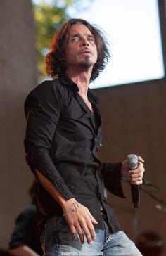 a man holding a microphone in his right hand and looking up at the sky while standing on stage