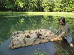 a man kneeling down in the water with some plants growing out of it and grass on top