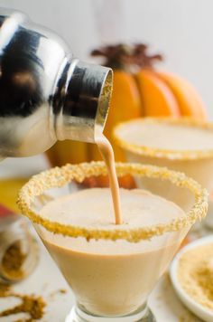 a person pouring something into a glass with another in the background and pumpkins behind it