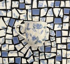 a blue and white coffee cup sitting on top of a mosaic tile wall covered in flowers