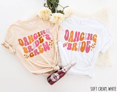 two t - shirts with the words dancing and brown on them are next to flowers