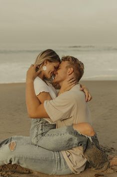 a man and woman are sitting on the beach hugging each other as they kiss in front of the ocean