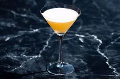 a glass filled with an orange drink on top of a black countertop next to a marble table