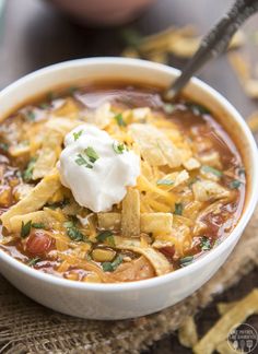 a bowl of chili soup with sour cream and tortilla chips on the side