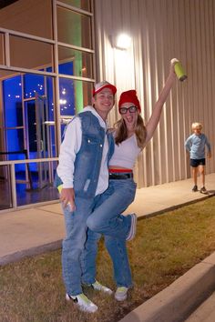 a man and woman posing for a photo in front of a building at night with their arms around each other