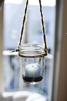 a mason jar filled with water and a lit candle hanging from a rope in front of a window