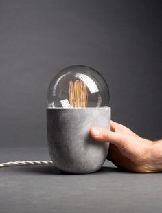 a hand holding a light bulb in front of a gray background with a white cord