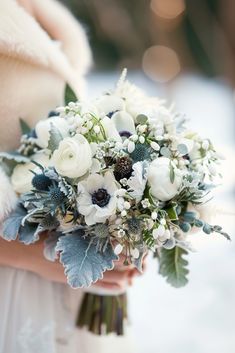 a bridal bouquet with white flowers and greenery is held by a woman's hand