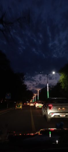 cars driving down the road at night with street lights in the background and clouds in the sky