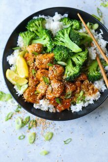 a black bowl filled with meat and broccoli on top of rice next to chopsticks