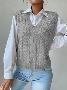 a woman wearing a gray sweater vest and white shirt with her hands on her hips