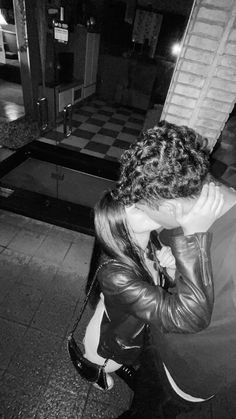 black and white photograph of woman in leather jacket on sidewalk at night with cell phone to her ear