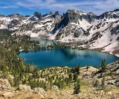 a lake surrounded by mountains with snow on the tops and trees in the foreground