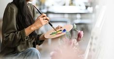 a woman sitting on the floor holding a paintbrush and palette