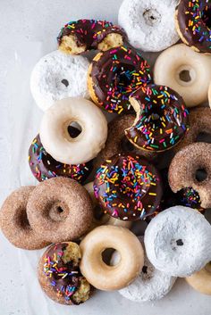 a bunch of doughnuts that are sitting on a white tablecloth with sprinkles