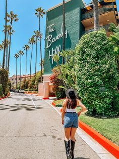 a woman in short shorts and cowboy hat walking down the street with palm trees behind her