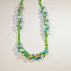 This dainty springtime necklace features three bundles of beaded daisies, woven in a spiral around multicolored green glass beads. The daisies come in shades of pink, blue, white, and cream, each with its own set of tiny leaves. This necklace looks beautiful at a variety of lengths, but was designed to be a choker (14-16in) or princess (18in) necklace. This necklace is made-to-order. Please allow 3-5 business days for processing. Spring Beaded Flower Necklace, Beaded Flower Necklace For Spring, Spring Flower Necklace With Colorful Round Beads, Spring Flower Necklace With Round Beads, Spring Beaded Flower Necklace With Round Beads, Handmade Flower Beaded Necklace For Spring, Spring Tiny Round Beaded Necklaces, Spring Flower Shaped Adjustable Beaded Necklaces, Spring Gift Beaded Necklaces With Tiny Beads