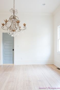 an empty room with a chandelier hanging from the ceiling and hard wood floors