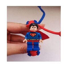 a hand holding a lego superman figure with a red cape on it's head