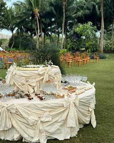 a table covered in white cloths sitting on top of a lush green field next to palm trees