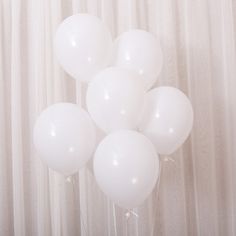 a bunch of white balloons sitting on top of a table next to a window curtain