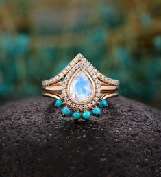 a gold ring with blue stones and a tear shaped diamond in the center, on top of a rock