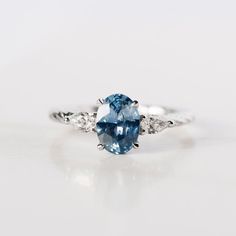 an oval blue and white diamond ring on a white surface with the center stone surrounded by three diamonds