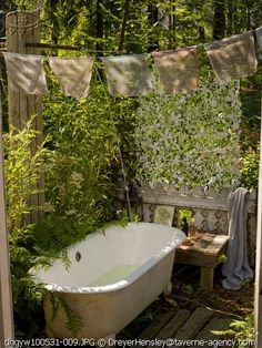 an old bathtub in the middle of a garden with clothes hanging from it's sides