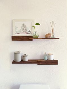 two wooden shelves above a white toilet in a bathroom with a plant on the wall