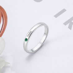 a close up of a ring with a green stone on it and flowers in the background