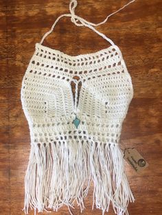 a white crocheted top with fringes hanging on a wooden table next to a tag