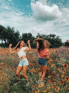 two girls are playing in a field full of wildflowers and one girl is holding her hair up